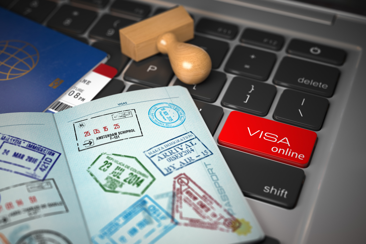 Open passport with visa stamps placed on a laptop keyboard featuring a red ‘VISA online’ key, symbolizing digital visa application.