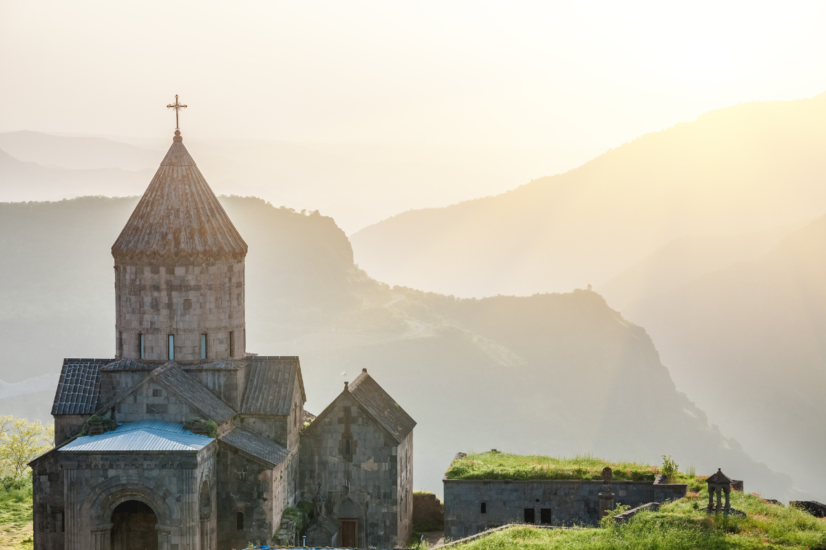 Tatev Monastery in southern Armenia surrounded by misty mountain views at sunrise.