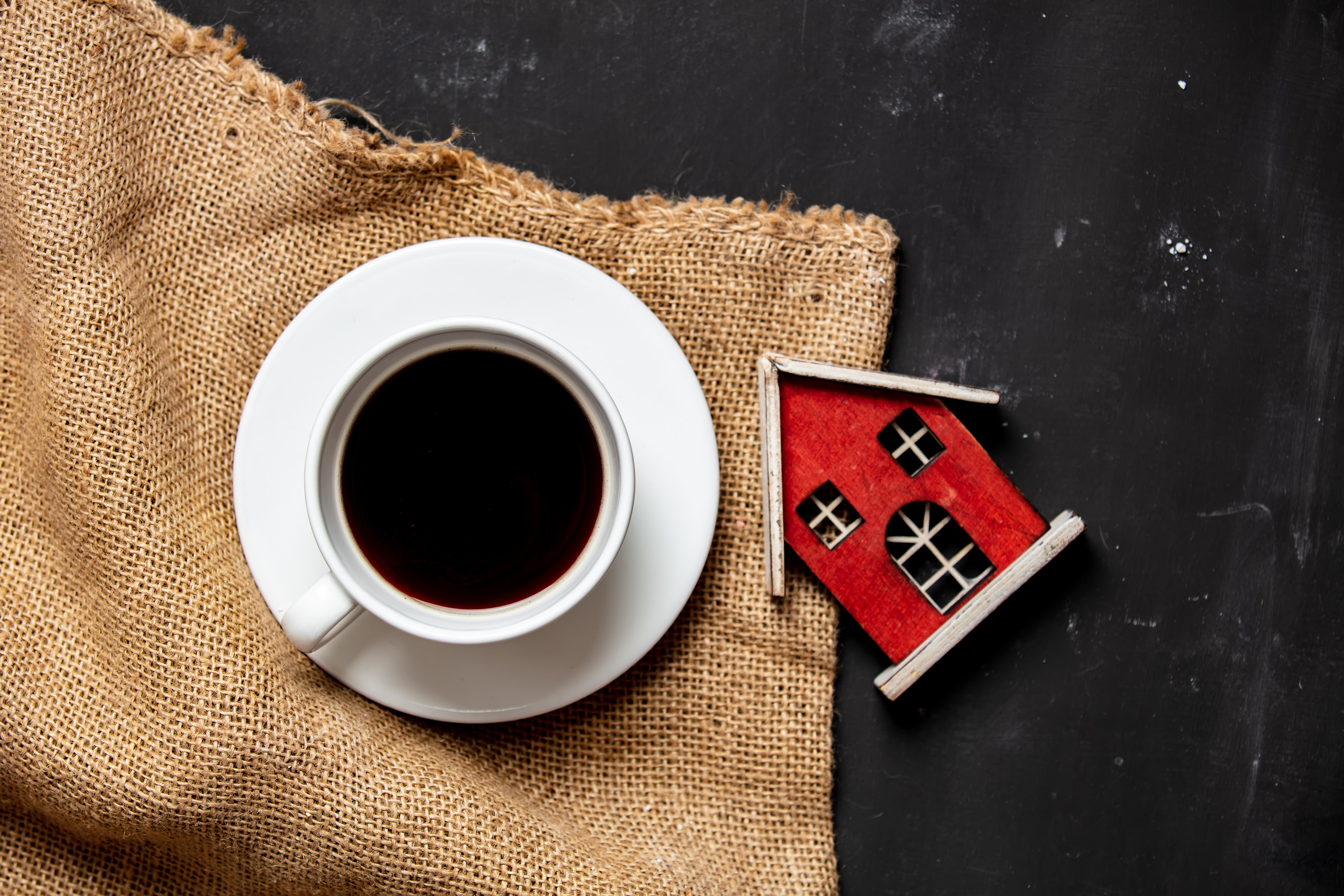 Coffee cup sitting on a burlap sack and a red village house carved out of wood